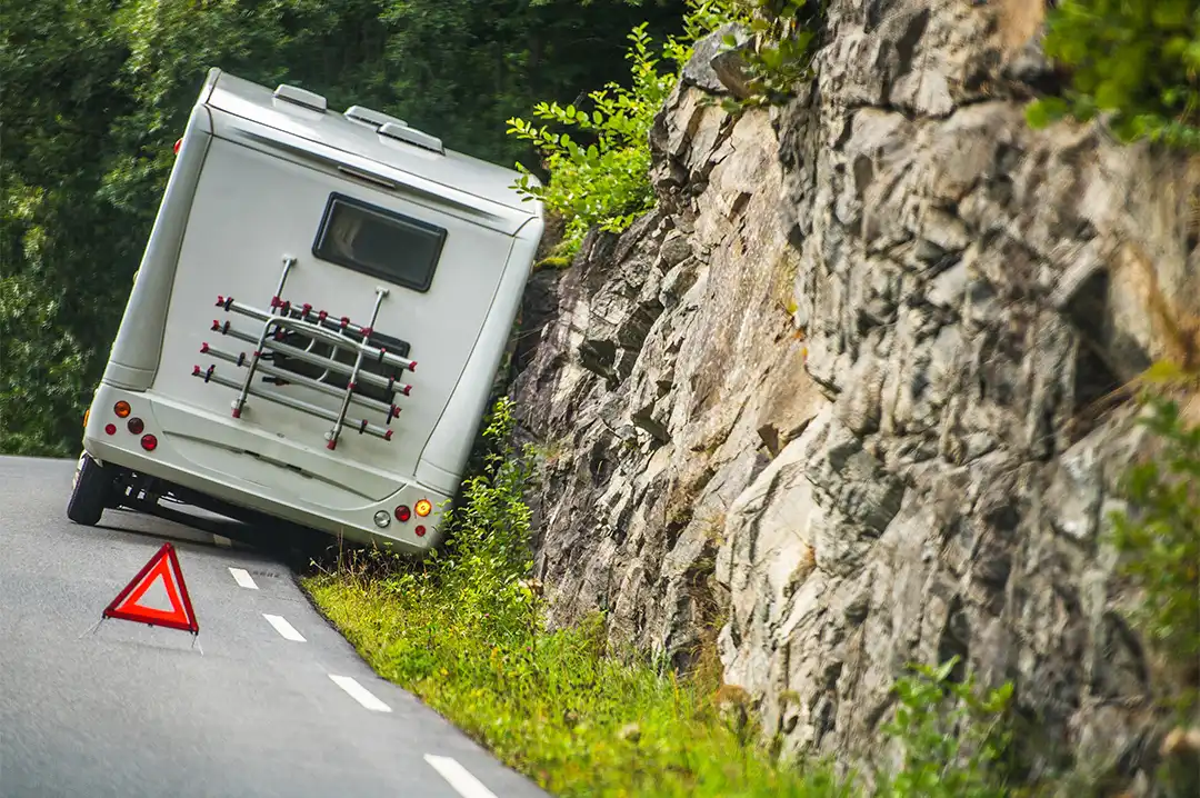 Ein Wohnmobil mit einer Panne steht am Straßenrand. Auf der Straße sieht man ein Warndreieck.