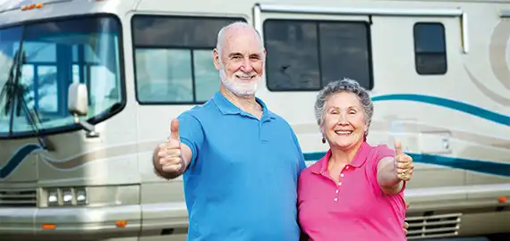 Ein Ehepaar im besten Alter stehen vor Ihrem Wohnmobil und halten Ihren Daumen hoch.