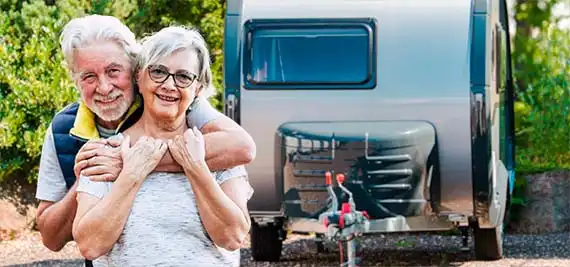 Ein Ehepaar im besten Alter stehen lächelnd vor einem Wohnwagen.